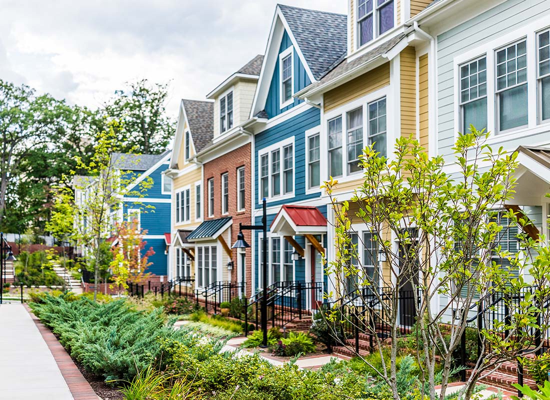 Homeowners Association Insurance - Row of Colorful, Red, Yellow, Blue, White, and Green Painted Residential Townhouses With Brick Patio in the Summer