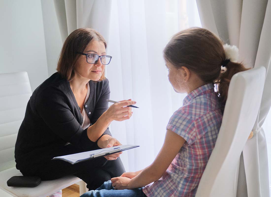 Social Services Agency Insurance - Social Service Employee With Glasses Talking and Offering Support to a Young Girl in Her Office Near a Window