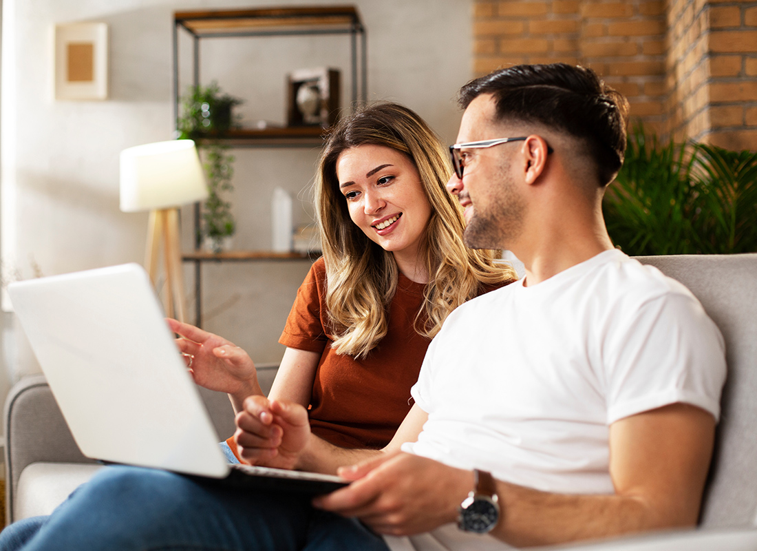 Blog - Couple Sitting on Couch in Home in the Living Room While Smiling and Pointing at an Open Laptop